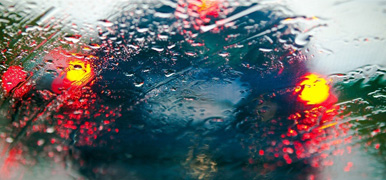 En blå bil skymtas genom en regntäckt bilruta